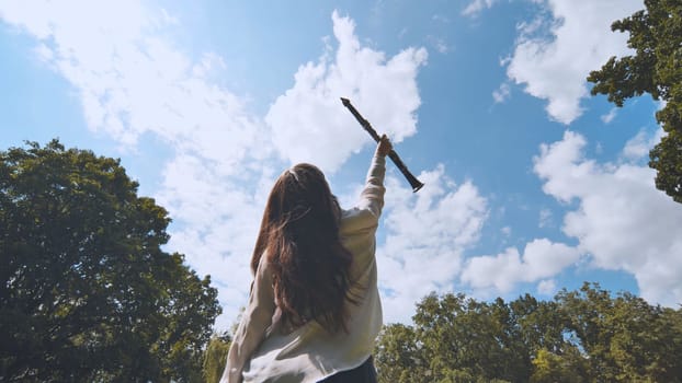 Young woman musician is raising a clarinet towards the sky in a park, celebrating music and nature
