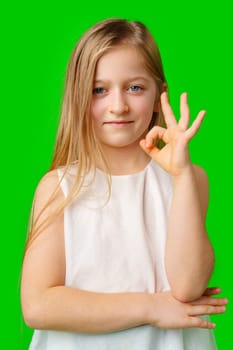 Young girl with long hair shows an okay hand gesture in front of a bright green background in studio