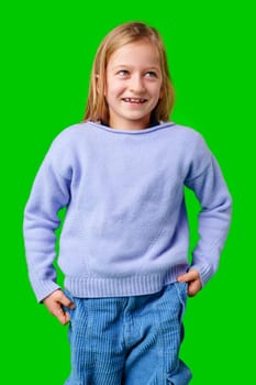 Child wearing a blue sweater and light blue pants stands confidently in front of a green background in a studio
