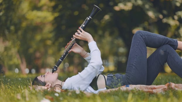 Musician reclining on green lawn, performing clarinet amid serene outdoor landscape, blending musical passion with natural surroundings