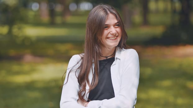 Portrait of a cheerful young georgian woman with long brown hair, enjoying a sunny day in a lush green park