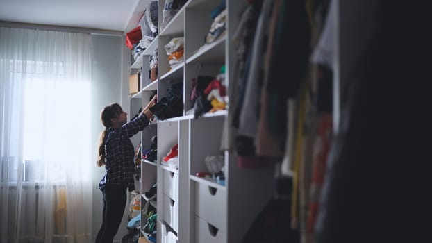 Young woman sorting wardrobe items, arranging clothing on shelves within spacious, minimalist walk in closet, maintaining clean personal storage area