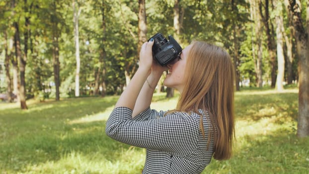 Professional female photographer capturing landscape through digital camera lens while standing in green urban park setting