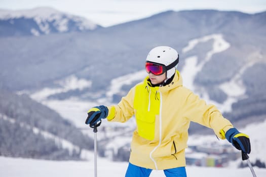 portrait of a skier in a mask and helmet with a closed face against a background of snow-capped mountains and blue sky,