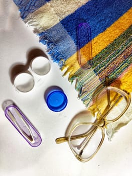Contact lens case, solution, and glasses are neatly arranged on a vibrant cloth, illustrating essential eye care items.