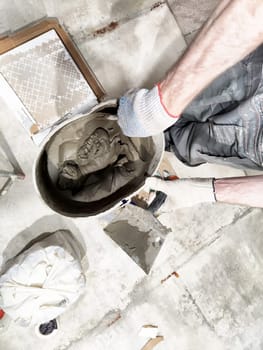 Worker is mixing concrete for indoor tile repair and installation on the floor, surrounded by tools and materials.