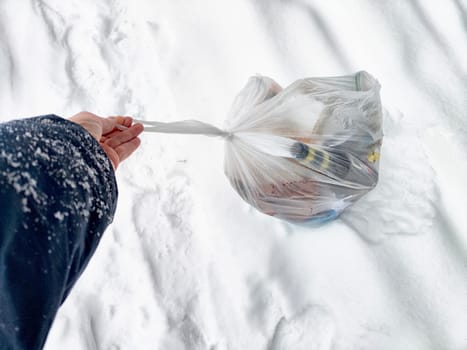 A person holds a garbage bag found in a snowy environment while hiking, highlighting a commitment to cleaning nature and reducing pollution.