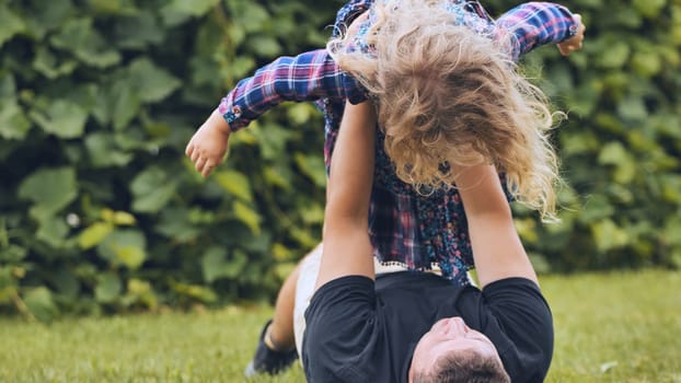 Father laughing, playing with smiling daughter among blooming garden flowers, sharing tender familial connection and happiness