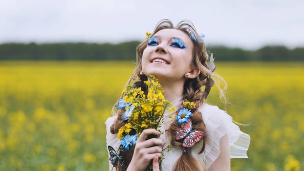 Portrait of a cheerful young blonde woman with flowers and butterflies in her hair holding a bouquet and enjoying spring in a blooming rapeseed field