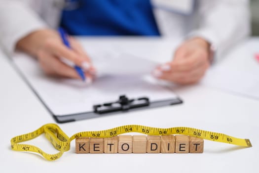 A professional reviewing a keto diet plan, with a measuring tape and blocks spelling Keto Diet prominently