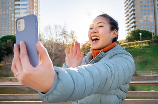 A joyful woman is engaging in a lively video call, wearing a bright smile, set against a sunny and vibrant background