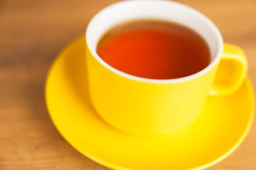 A yellow cup and saucer in which black tea is poured close-up on a wooden background. The concept of tea drinking, tea traditions. High quality photo