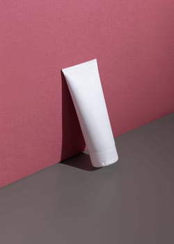 Whate blank squeeze cream tube on a grey and dark red background with hard shadow closeup, cosmetic mockup, negative space. Skincare beauty product for facecare and spa, minimal aesthetic