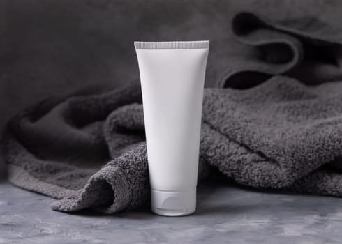 White blank cosmetic squeeze cream tube on dark grey towel in bathroom closeup, brand packaging mockup, copy space. Natural handmade cosmetic product for facecare and spa procedures