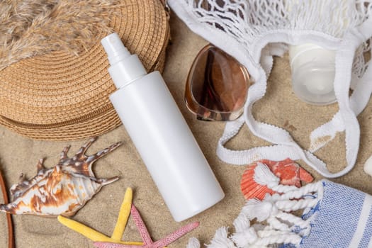 White blank spray bottle, sunglasses, towel, starfishes and shells on a sandy beach, top view. Sunscreen cosmetics mockup. Summer vacation and spf uv-protecting skin care concept