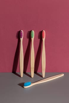 Multicolor bamboo toothbrushes on a grey and dark red background with hard shadow closeup, mockup, negative space. Natural hygiene accessories for dental care, minimal style aesthetic