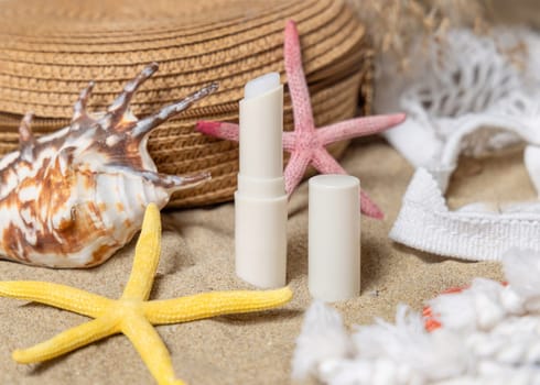 Opened sunscreen lip balm stick near starfishes and seashells on a sandy beach, top view. Sunscreen cosmetics mockup. Summer vacation and spf uv-protecting lip care concept