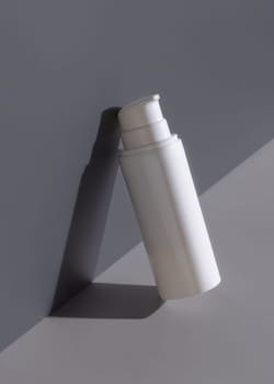 Blank white one pump cream bottle on a grey and dark red background with hard shadow closeup, cosmetic mockup, negative space. Skincare beauty product for facecare and spa - lotion or toner, minimal aesthetic