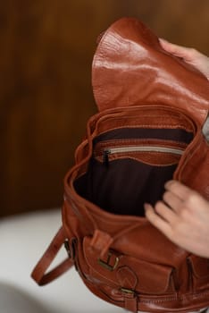 beautiful girl in gray pants and beige sweater posing with a small brown leather backpack.