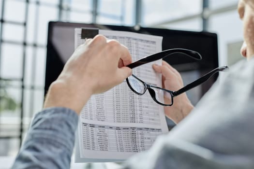 Close-up of a financial businessman holding an information sheet in his hands, reading the company's financial statements for making a financial plan.