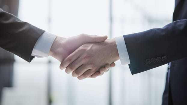 Close up of handshake on blurry conference room interior background. Partnership concept