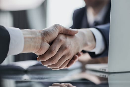 Close up of greeting handshake, young businessman hands shaking over conference table