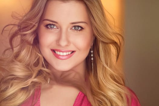 Woman with blue eyes and long, voluminous blonde hair styled in soft curls, wearing pink dress and elegant earrings, dreamy and feminine look idea