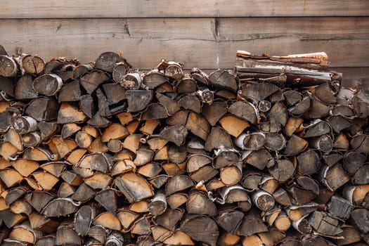 Firewood logs stacked and drying near a wooden wall in a rural area of russia, creating a rustic and traditional scene