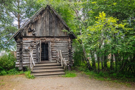 Historic wooden cabin featuring ornate woodwork, birch railing surrounded by verdant forest landscape, embodying rustic serenity