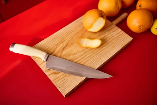 A cutting board with a knife and oranges, captured on a vibrant red background.