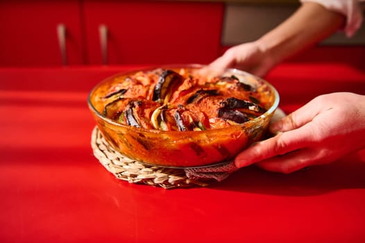 Delicious vegetable casserole freshly baked and served on a rustic table setting. A vibrant red background enhances the colorful dish, making it appealing and appetizing, emphasizing its homemade preparation.