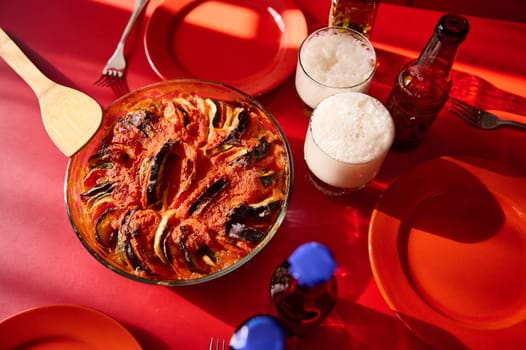 A colorful presentation of a ratatouille-style vegetable dish with beverages on a red table setup.
