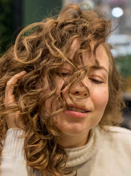 girl in a beauty salon after styling with a gorgeous hairdo. hair shown close-up, girl's face close-up. large wavy curls. girl fixes her hair with her own hands