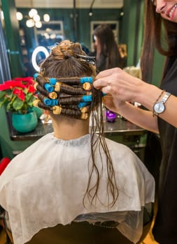 a young girl is getting her hair curled with curlers by a hairdresser. the client is sitting in a chair in a beauty salon. her hair is being styled. her hair will be curly and wavy