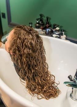 client's hair is washed in a beauty salon. we see a white sink and beautiful curly hair of the client's girl. hair is long and wavy after the procedure of styling and hair treatment