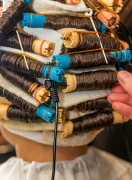 modern process of hair treatment and curling. client sits in chair with curlers on her head. device treats and makes hair curly and wavy. master adjusts curlers, close-up