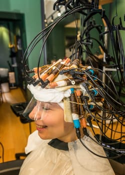 a young girl is getting her hair curled with curlers. the client is sitting in a chair with a lot of curlers on her head. hardware treatment and hair curling are being performed.
