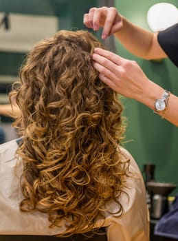 girl in a beauty salon after styling with a great hairdo. hair is shown close-up, client is seen from behind. large wavy curls. the master adjusts the client's curls with her hands