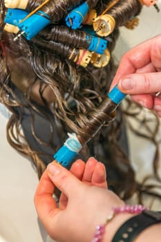 the hairdresser removes curlers from the client's hair. close-up of the client's head, and the hairdresser unwinds the hair. the client will have wavy hair and beautiful curls