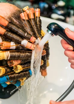close-up in a beauty salon, they wash their hair. The master rinses the solution from the client's hair with water. There are curlers on the hair, the hair curling process is underway