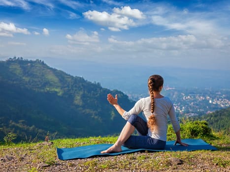 Hatha yoga outdoors - sporty fit woman doing yoga asana Parivrtta Marichyasana (or ardha matsyendrasana) - seated spinal twist outdoors in mountains in the morning