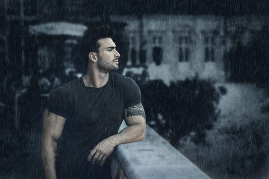 A man leaning on a rail in the rain. Photo of a ruggedly handsome man leaning on a rain-soaked rail