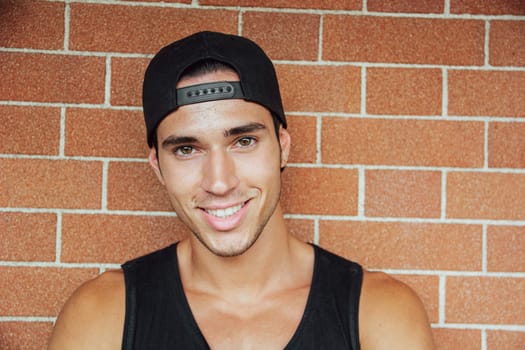 A man in a black shirt and a black hat. Photo of a stylish and handsome young man wearing a black shirt and hat smiling to the camera