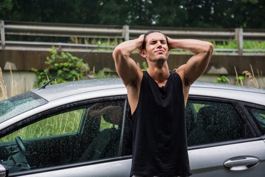 A man standing next to a car in the rain, sad because his vehicle broke down