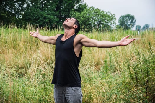 A man standing in a field with his arms outstretched. Photo of a man standing in a field with his arms outstretched in a freedom or liberation concept