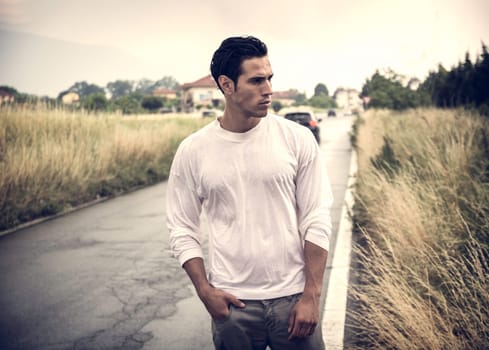 A man standing on the side of a road next to tall grass