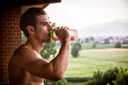 young and attractive muscular shirtless man enjoying a colorful protein shake