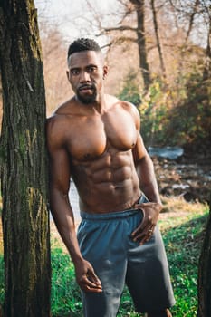 A shirtless man standing next to a tree. Photo of a shirtless man standing next to a tree in a natural setting