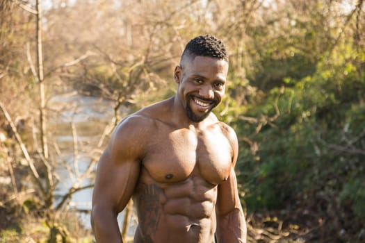 A shirtless man standing in a field next to a small water stream. Photo of a shirtless man standing in a field next to a body of water