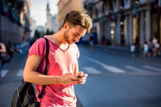 A man standing on a street looking at his cell phone. Photo of a man engrossed in his cell phone on a busy city street